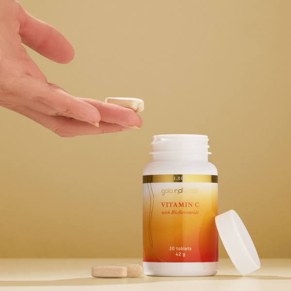 Vitamin C supplement bottle with a hand holding a tablet against a beige background, GAIA NATURELLE
